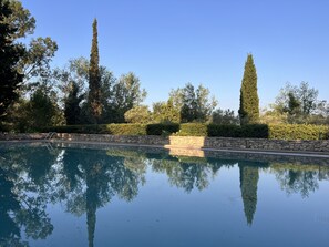 Une piscine aux eaux cristallines, bordée de murs et d’un escalier en pierre qui y mène, le tout entouré d’arbres et d’arbustes.