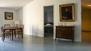 A dining area with a wooden table and chairs, a dresser with drawers, a framed portrait on the wall, and a bed in the adjacent room. - Comfort Suite for 4 people (Tarascon)