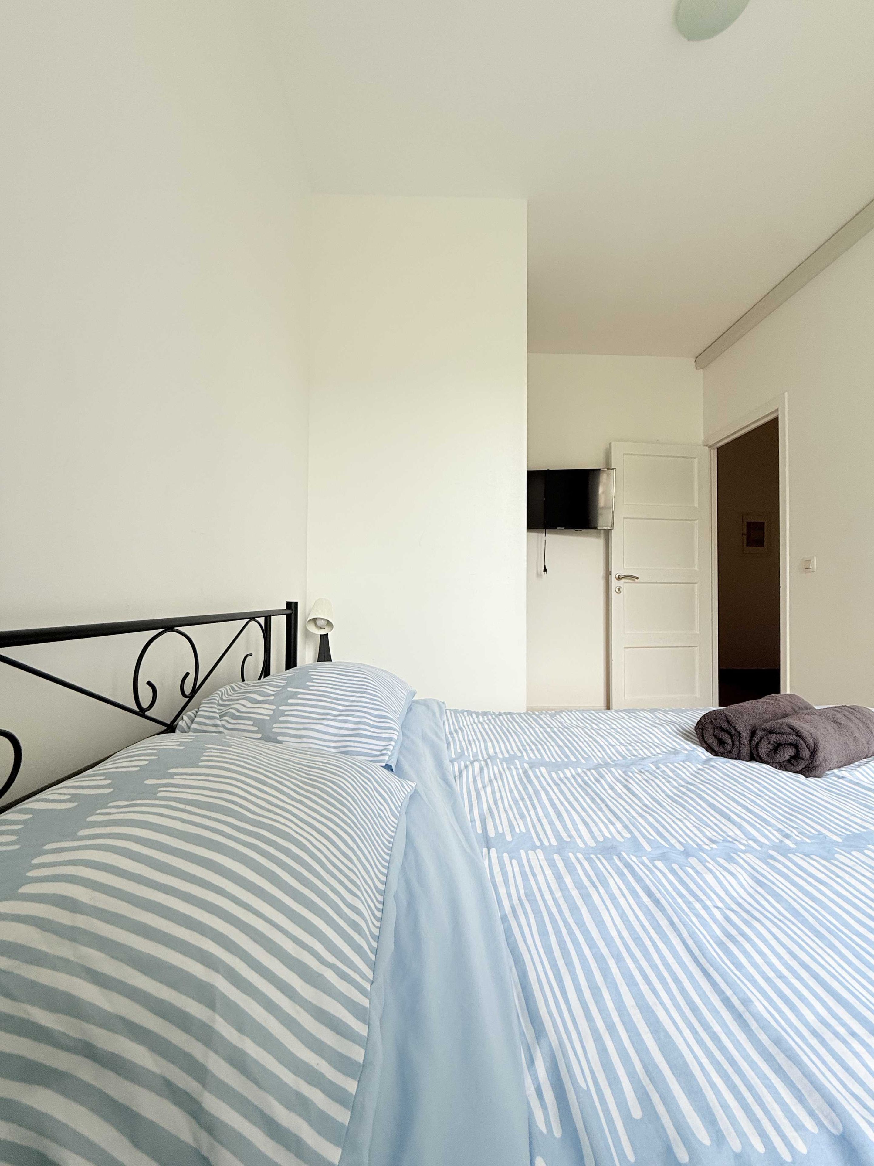 A bedroom with a bed, a door, and a wall-mounted TV.