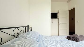 A bedroom with a bed, a door, and a wall-mounted TV.