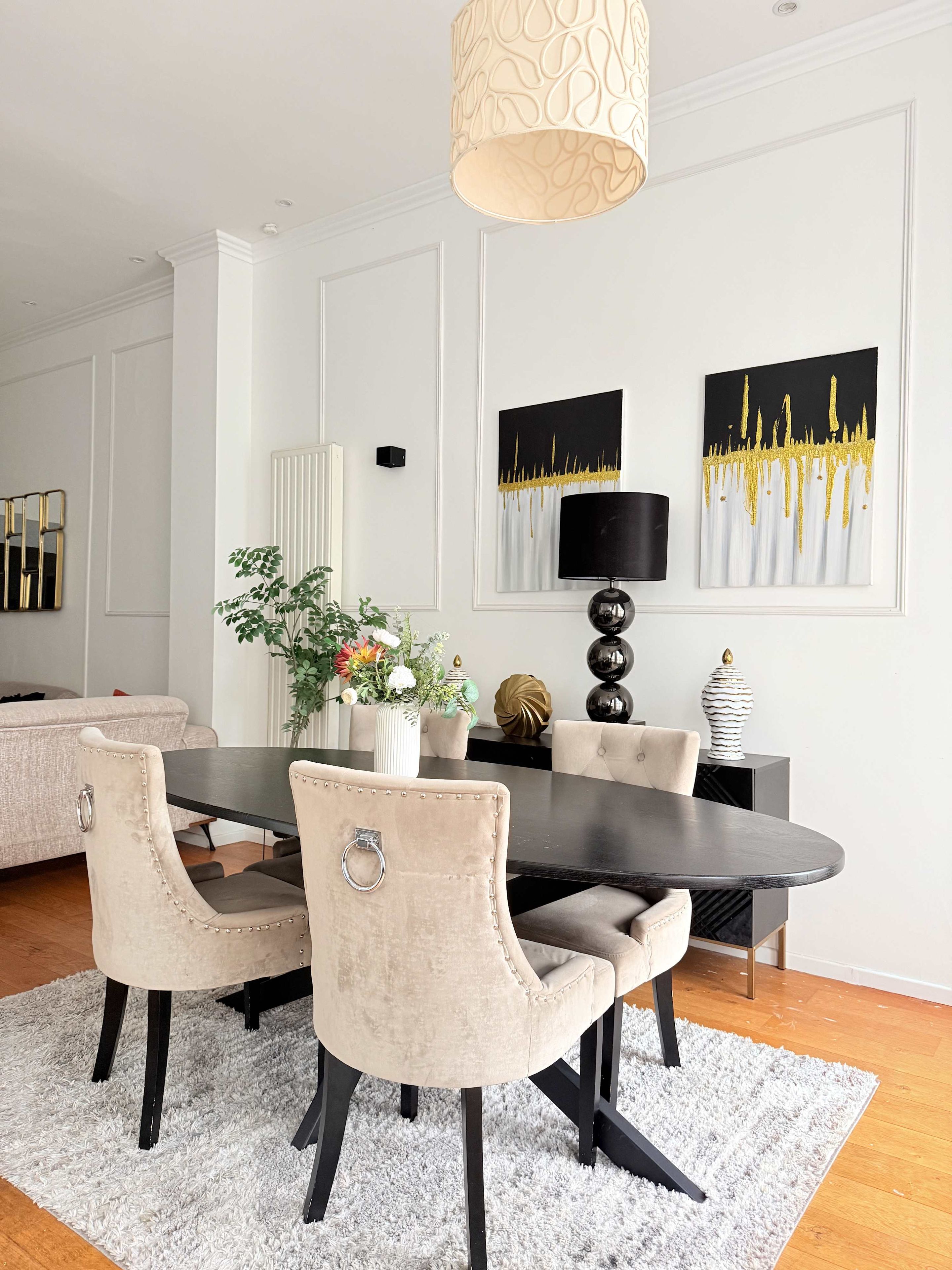 Een eetruimte met een donker houten tafel, beige stoelen met bekleding, een wit tapijt en een hanglamp.