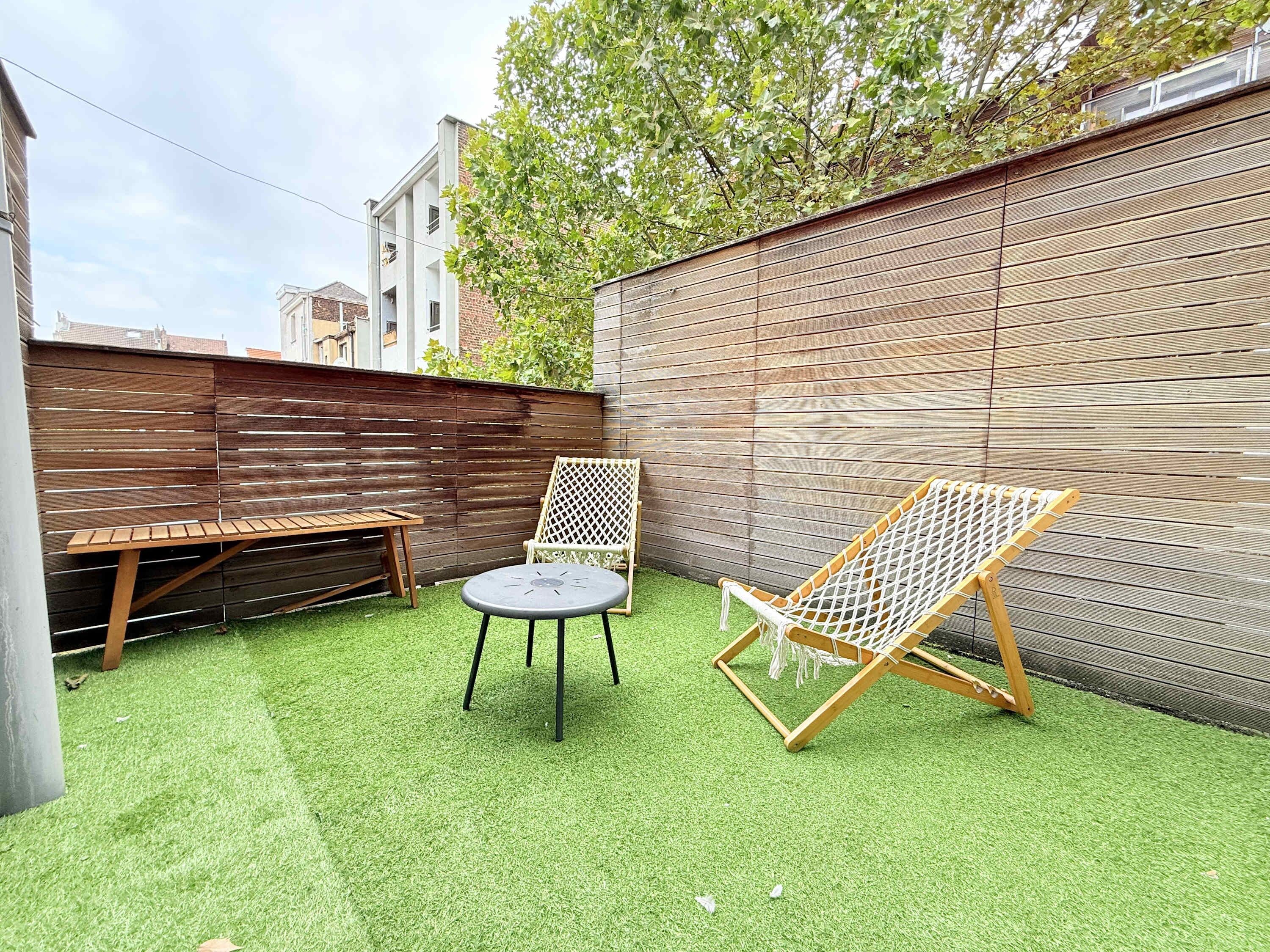 A backyard with artificial grass, a wooden bench, a wicker chair, and a hammock.