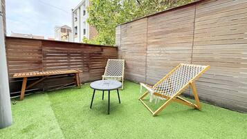 A backyard with artificial grass, a wooden bench, a wicker chair, and a hammock.