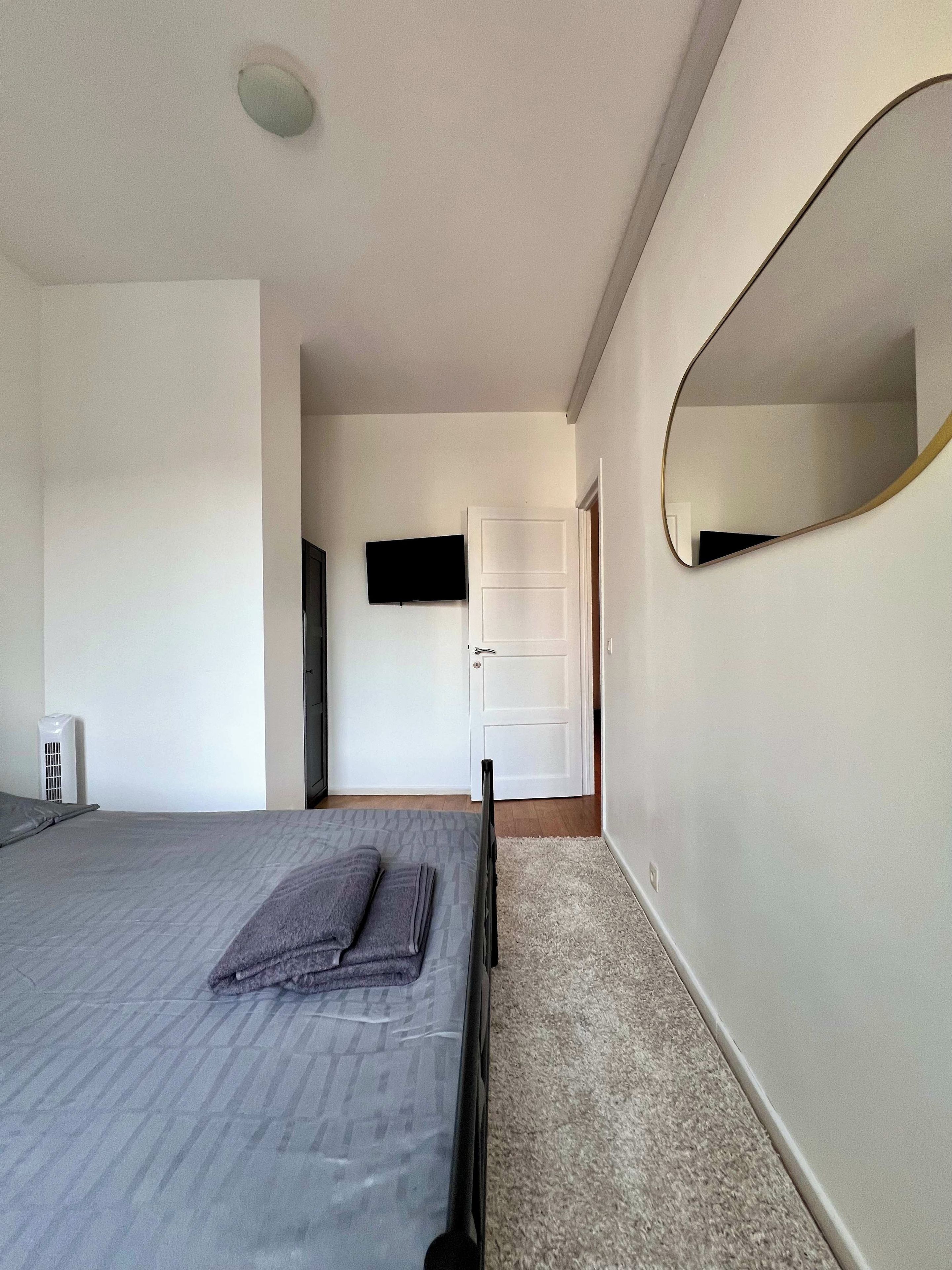 Een slaapkamer met een bed, een flatscreen televisie aan de muur, een deur en een grote spiegel.