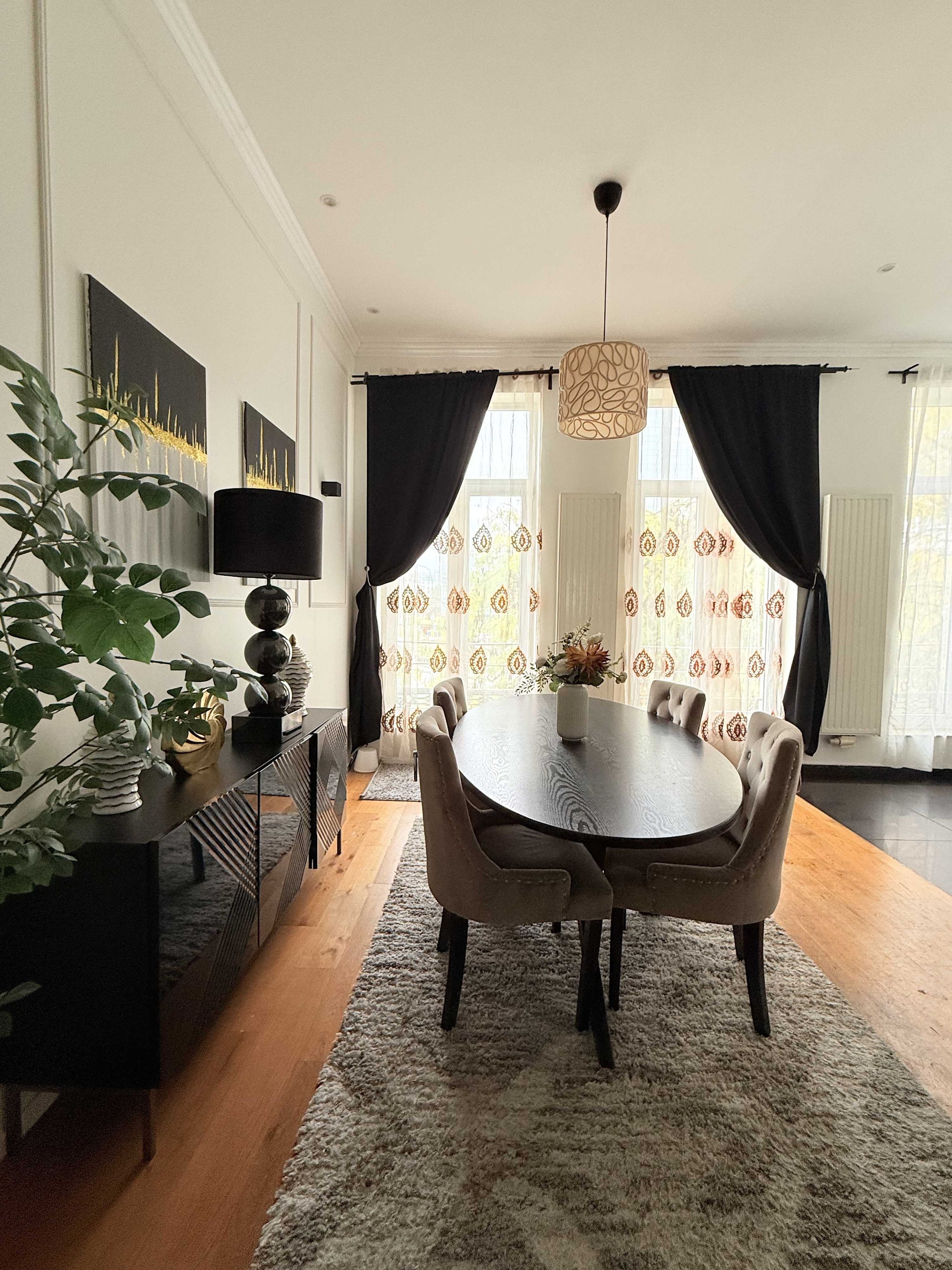 A dining area with a round table, chairs, a vase with flowers, and a plant on the side.