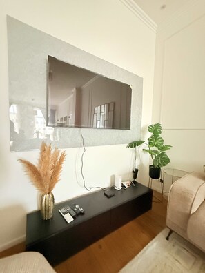 Ein modernes Wohnzimmer mit einem Wandfernseher, einem schwarzen Konsolentisch, einem Blumentopf und einer dekorativen Vase.