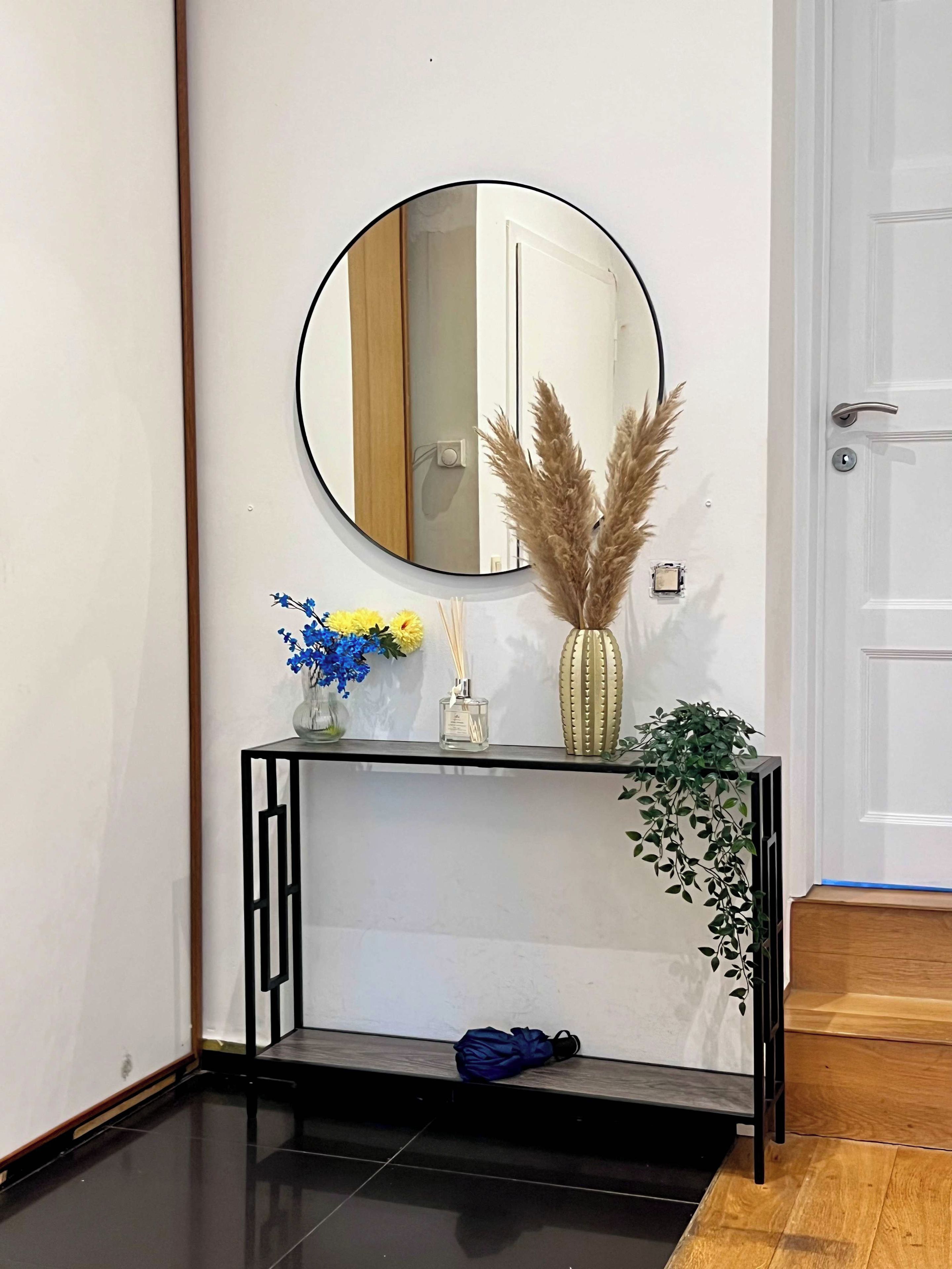 Une console agrémentée d’un miroir, de vases et d’objets décoratifs, le tout placé devant un mur blanc.