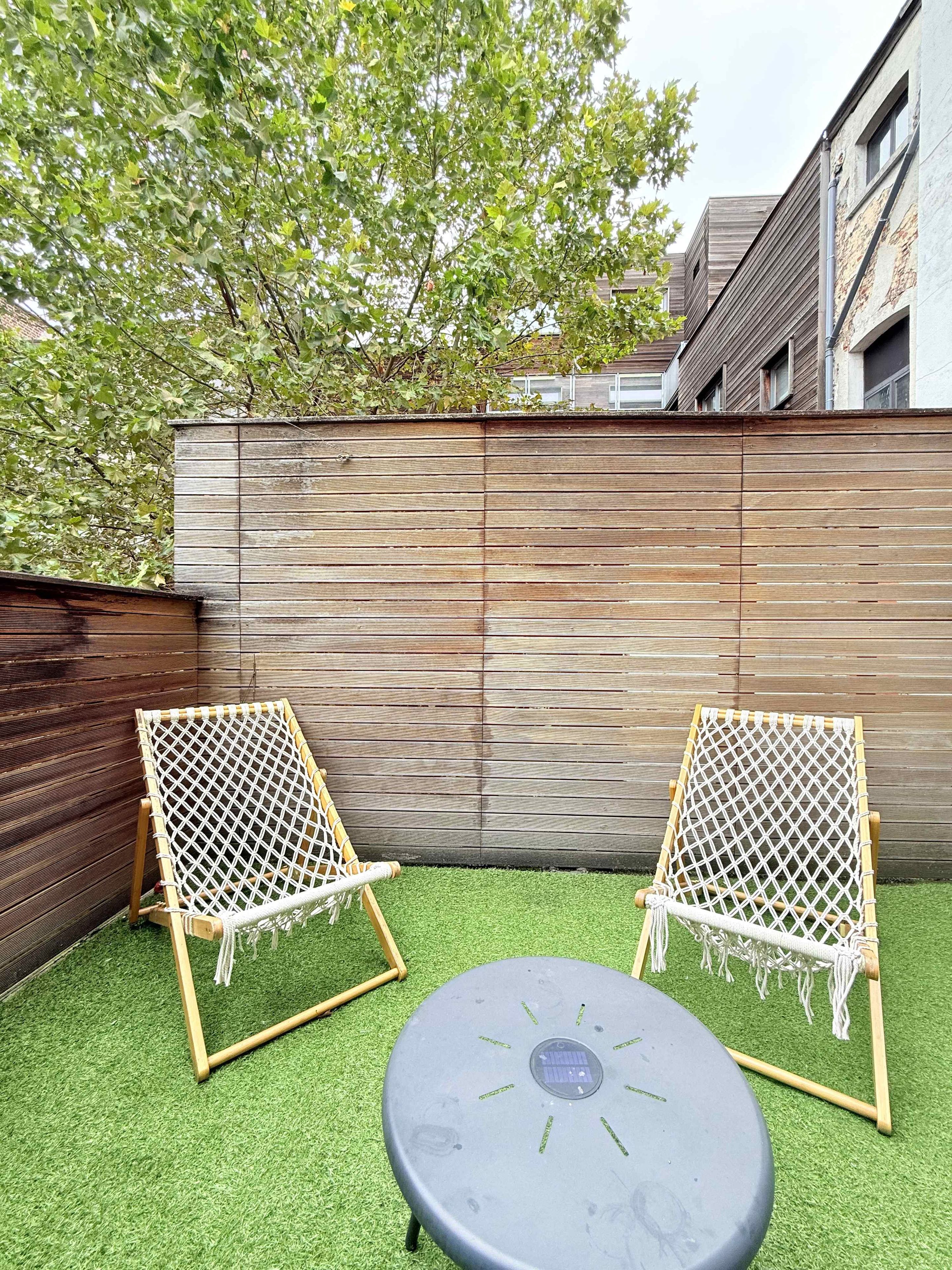 A backyard with two hammock chairs and a round table on artificial grass.