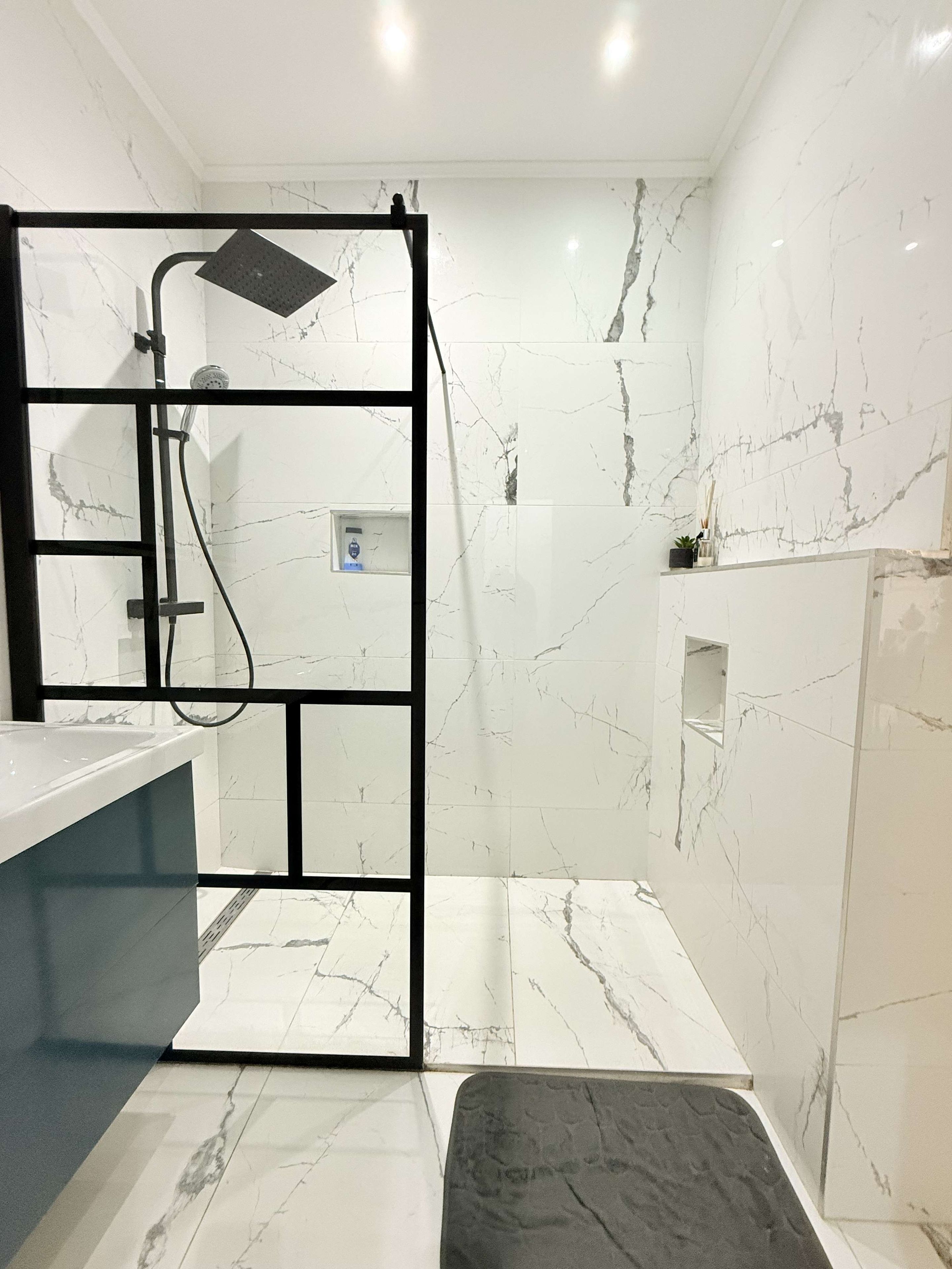 Een moderne badkamer met douchecabine, wastafel en marmeren vloer.