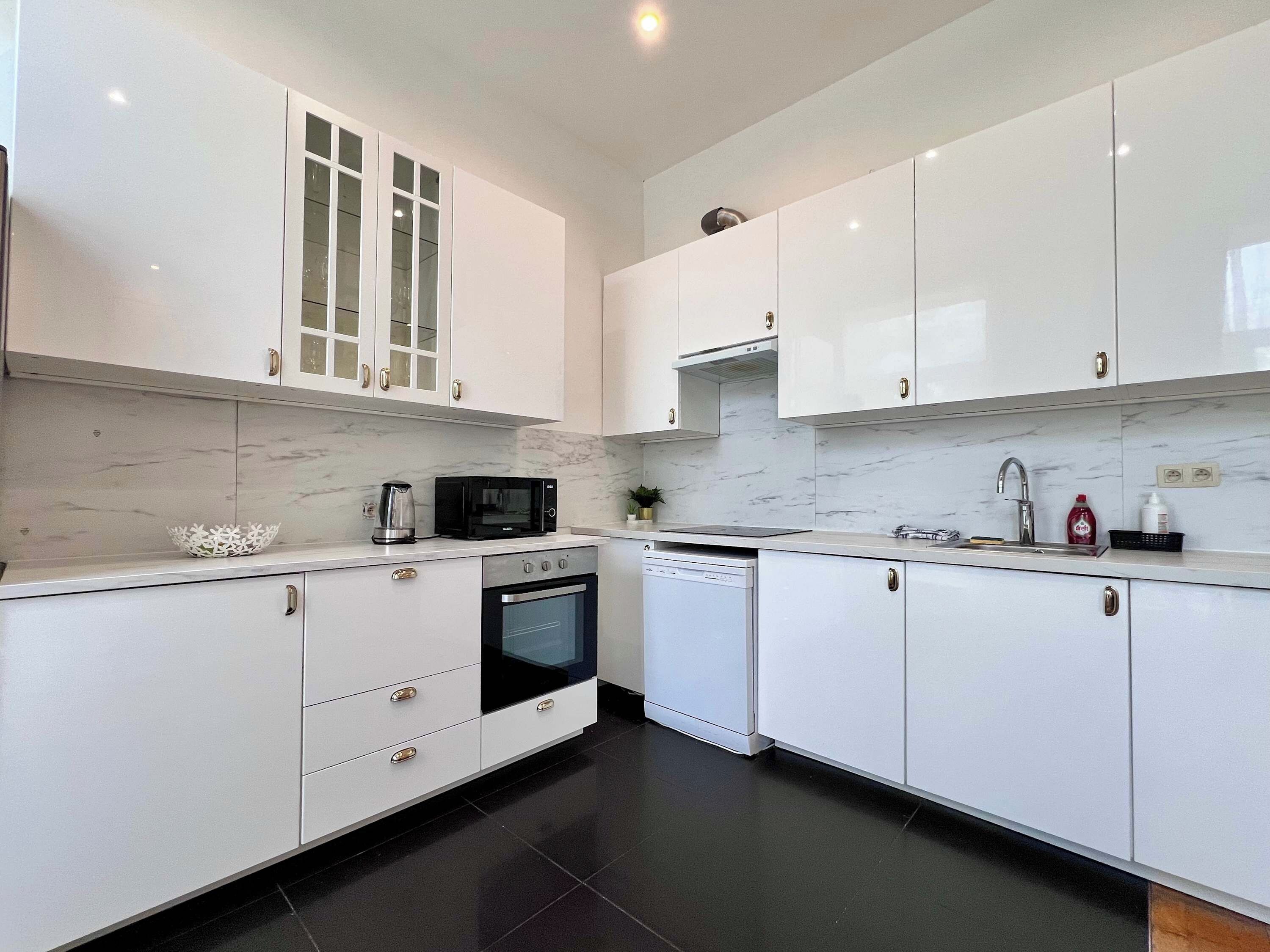 Une cuisine moderne avec des meubles blancs, un four à micro-ondes, un four traditionnel et un lave-vaisselle.