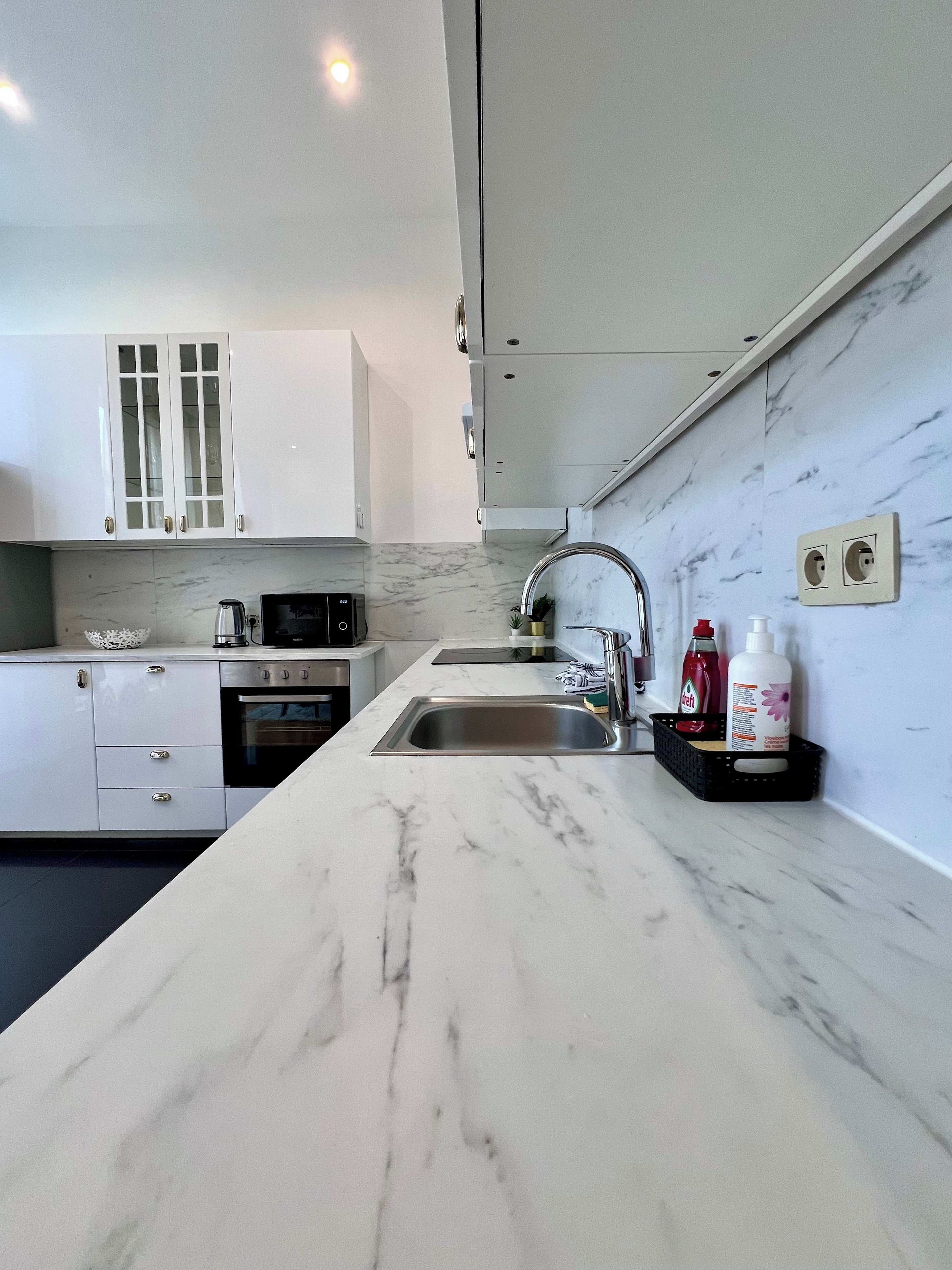 Een moderne keuken met een marmeren aanrechtblad, een roestvrijstalen spoelbak en witte kasten.