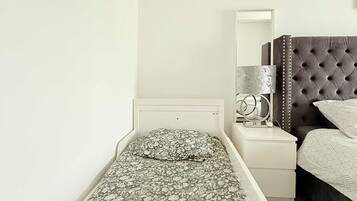 Een eenpersoonsbed met een bloemenprint sprei, een nachtkastje met een lamp en een donker beklede hoofdbord.