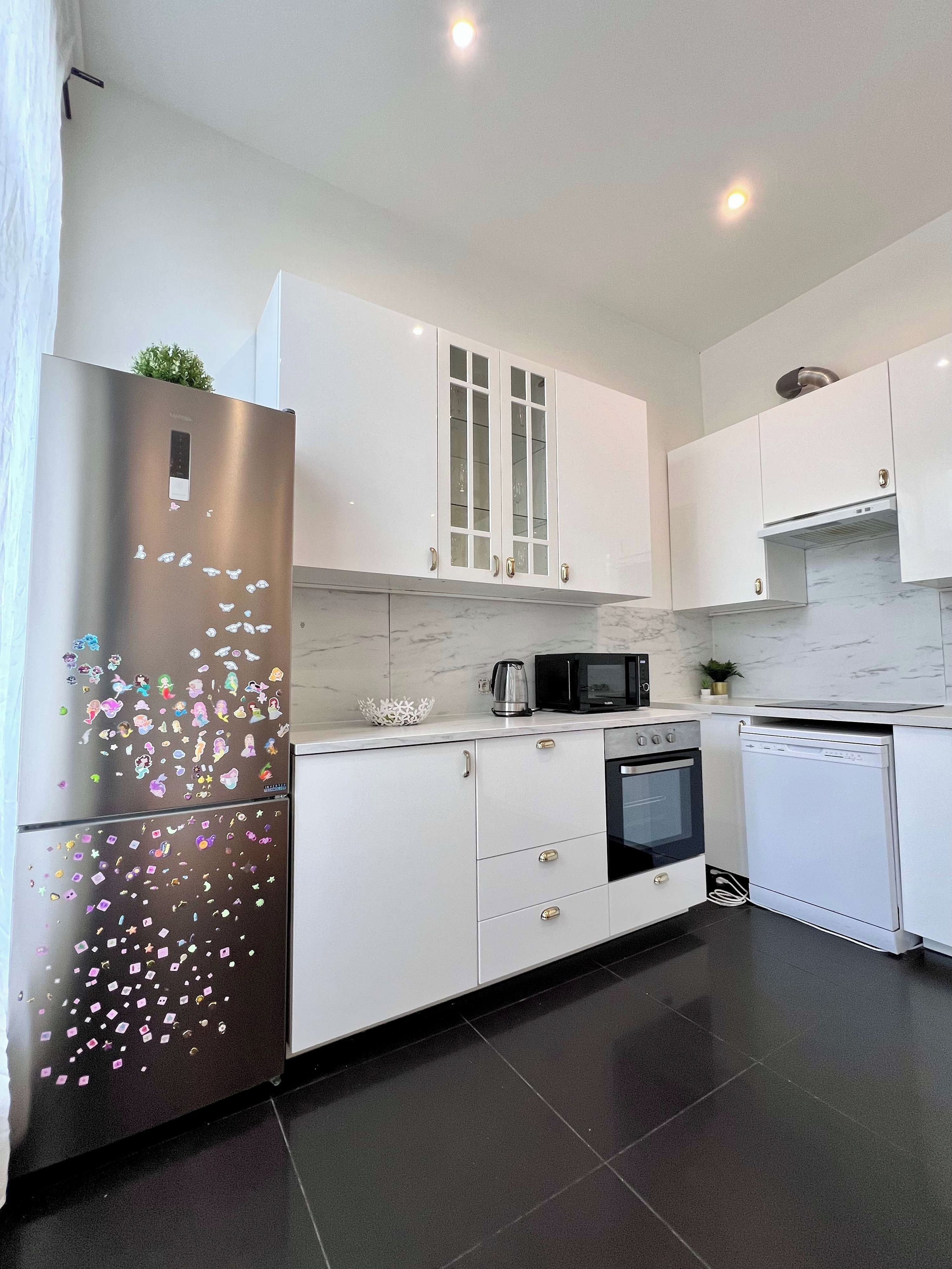 Une cuisine moderne avec des meubles blancs, des appareils en acier inoxydable et un sol carrelé.