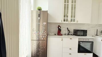 Een moderne keuken met witte kasten, een roestvrijstalen koelkast, een magnetron en een oven.