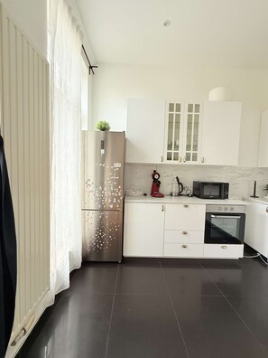 A modern kitchen with white cabinets, a stainless steel refrigerator, a microwave, and an oven.