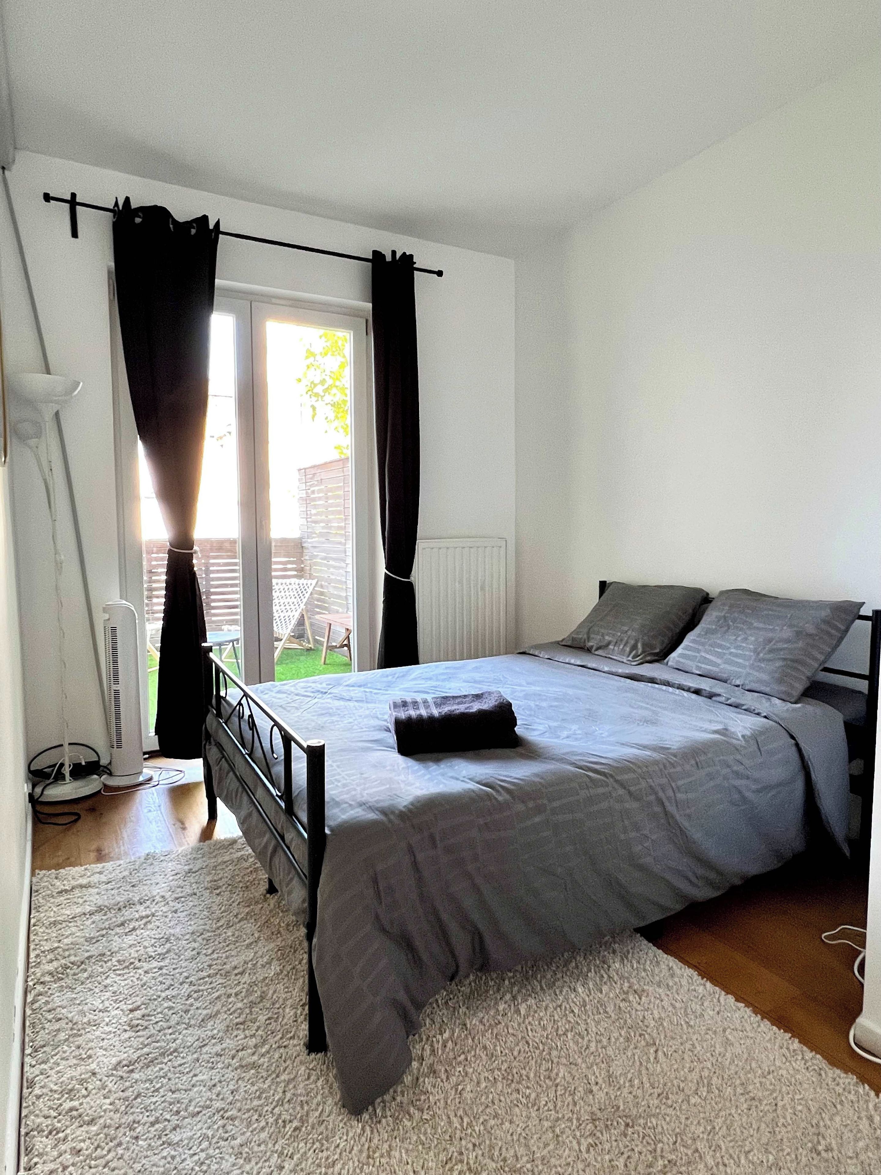 Een slaapkamer met een bed, een radiator, een raam met gordijnen en uitzicht op buiten.