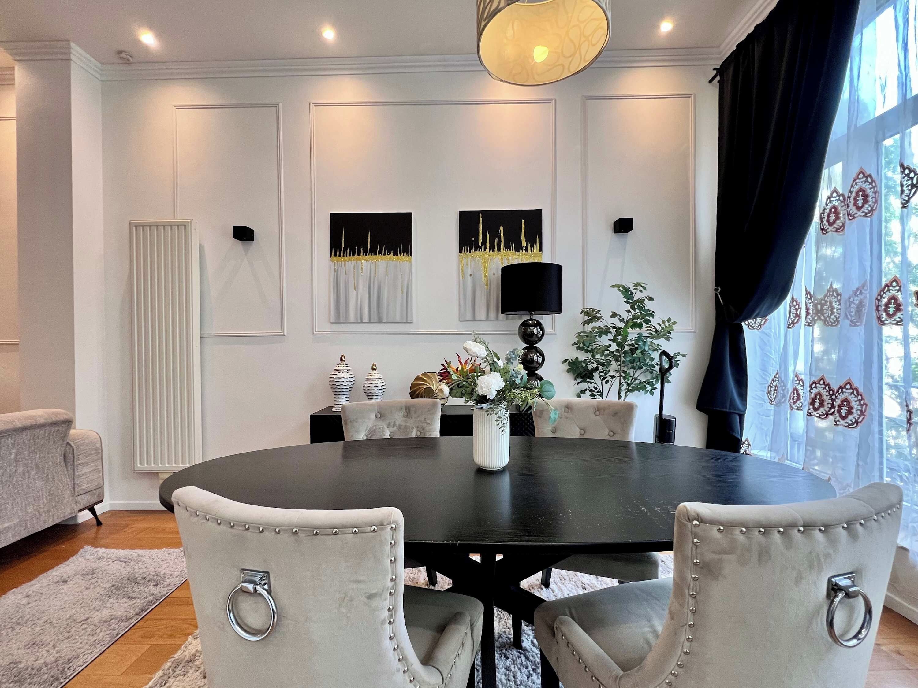 Een eetkamer met een ronde tafel, vier gestoffeerde stoelen, een vaas met bloemen en wanddecoratie.