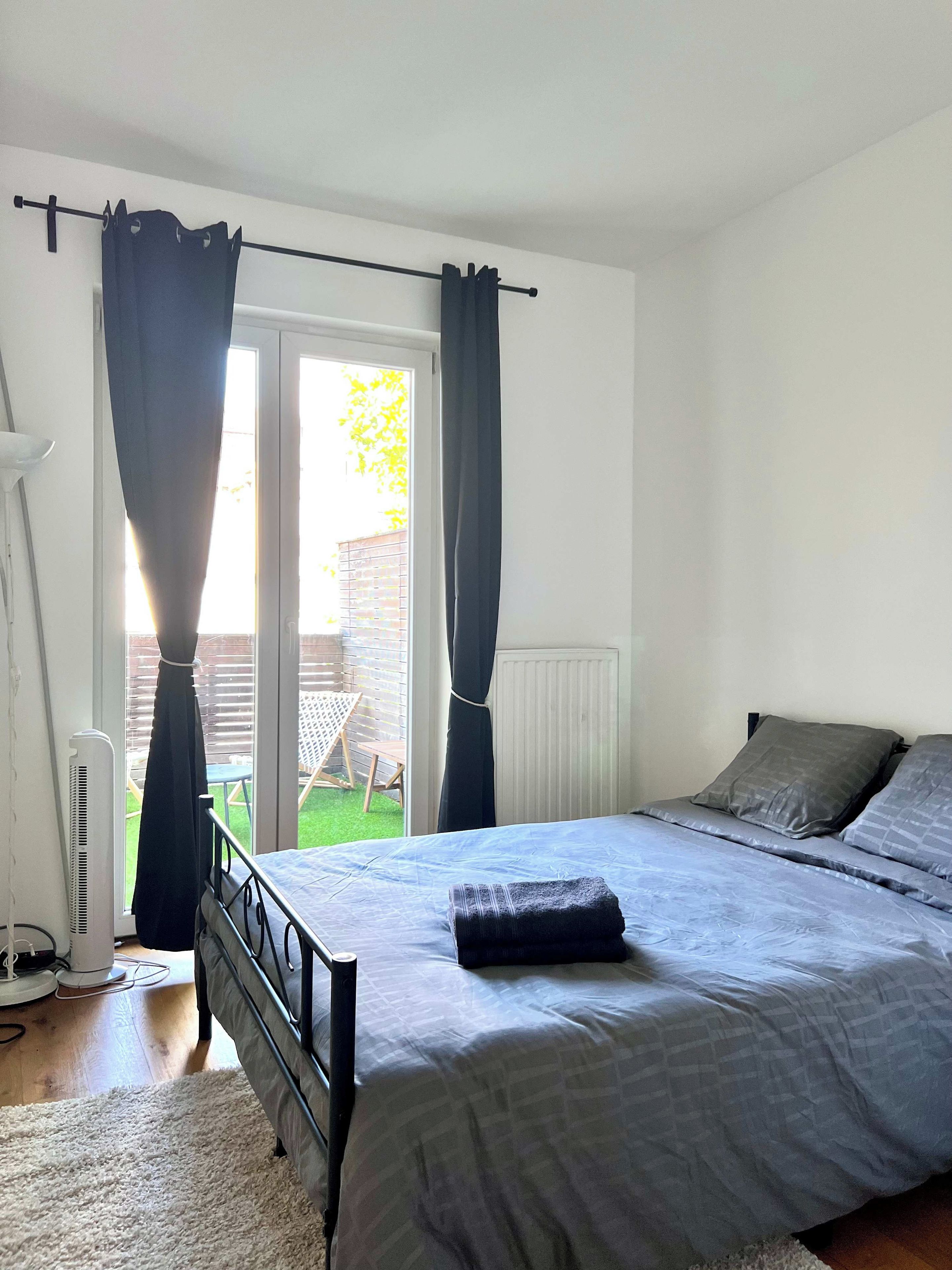 Une chambre à coucher avec un lit, des rideaux, un radiateur et une vue sur l’extérieur.