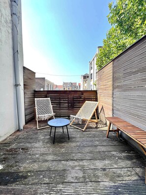 An outdoor seating area with a round table and two chairs, a wooden bench, and a metal fence.