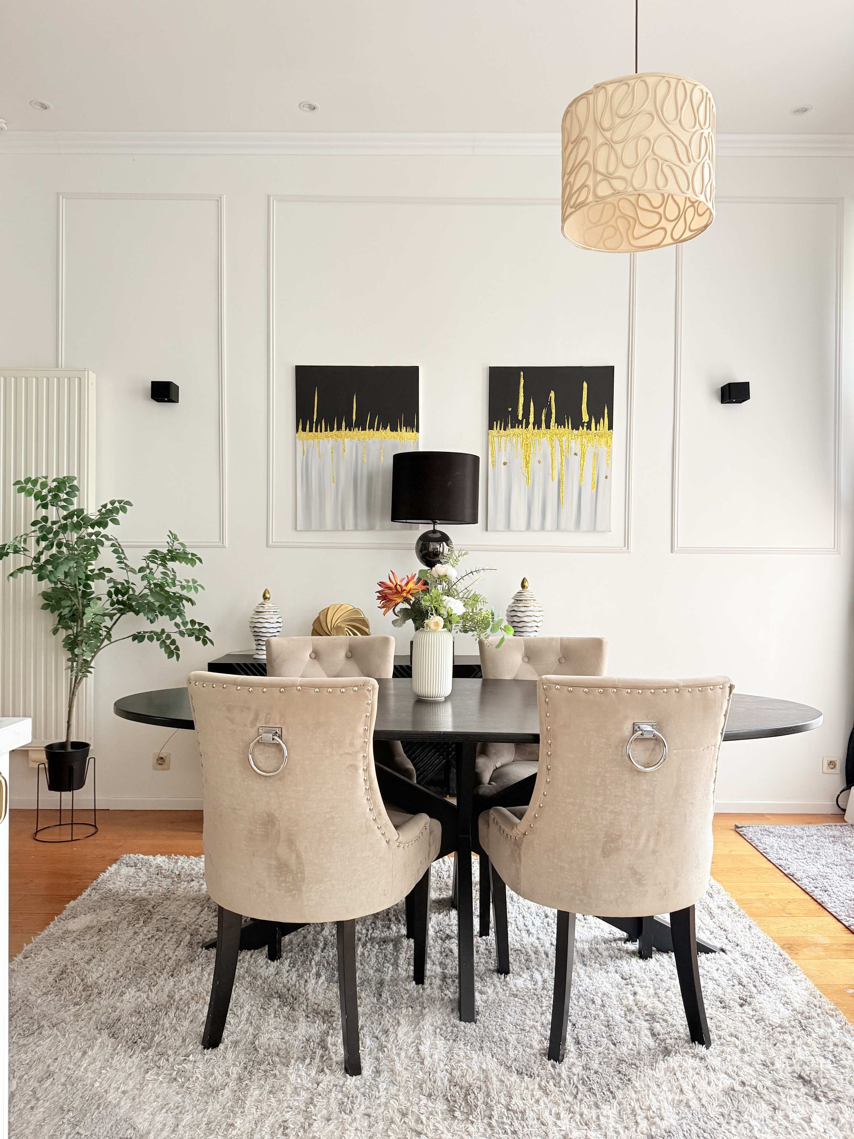 Een eethoek met een ronde tafel, vier stoelen, een vaas met bloemen en twee aan de muur hangende schilderijen.