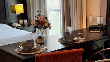 Ett hotellrum med ett välordnat matbord dukat för två personer, en vas med blommor, en sänglampa och en säng med ett vitt överkast.