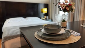 Ein ordentlich bezogenes Bett mit weißen Leinen, ein Nachttisch mit einer Schale und einem Glas sowie eine Vase mit Blumen.