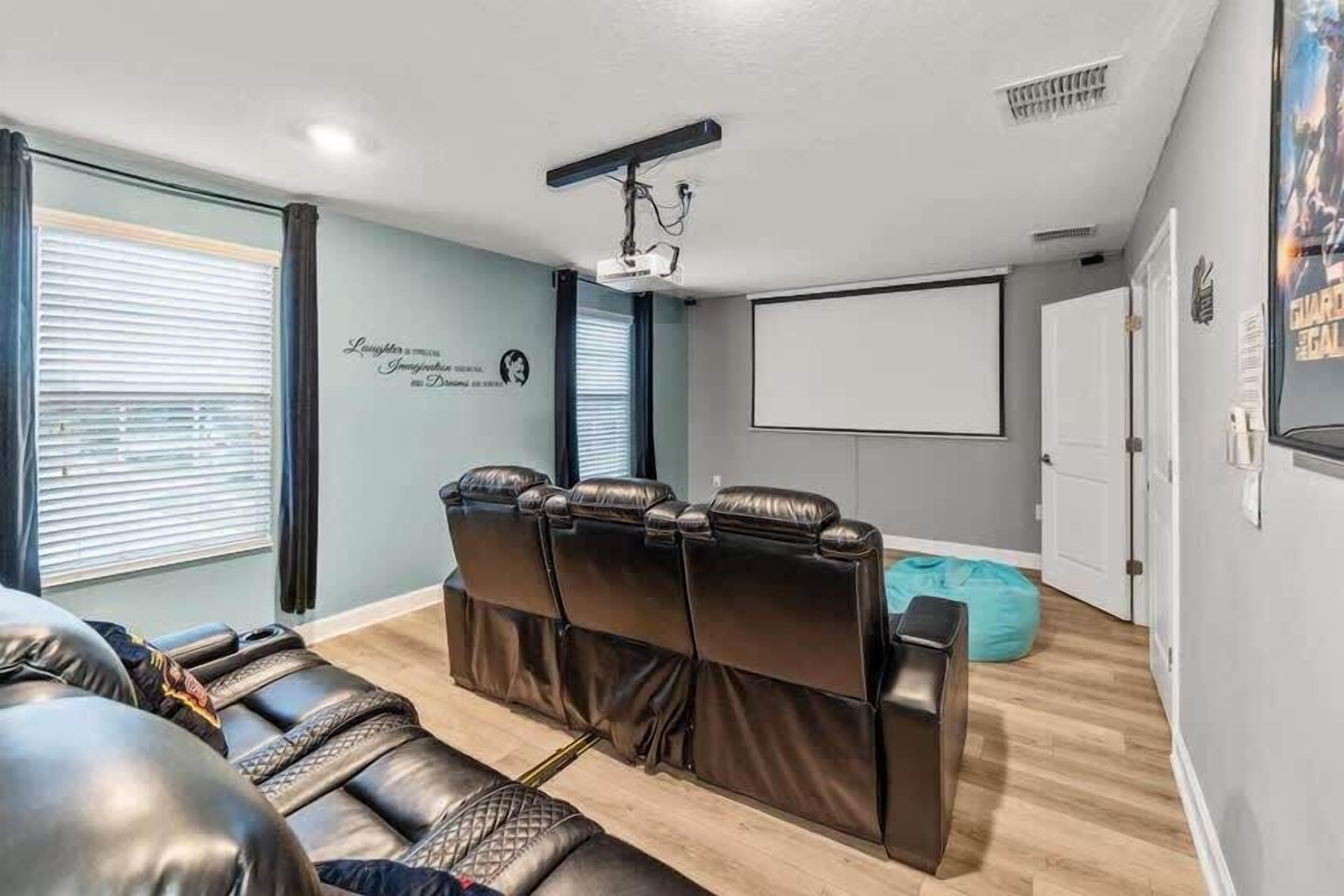 A home theater room with a reclining sectional sofa, a large screen, and a projector.