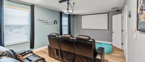 A home theater room with a reclining sectional sofa, a large screen, and a projector.
