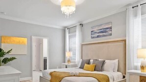 Ein Schlafzimmer mit Bett, Nachttischen, einem Chandelier, einem Gemälde und einem Fenster mit Vorhängen.