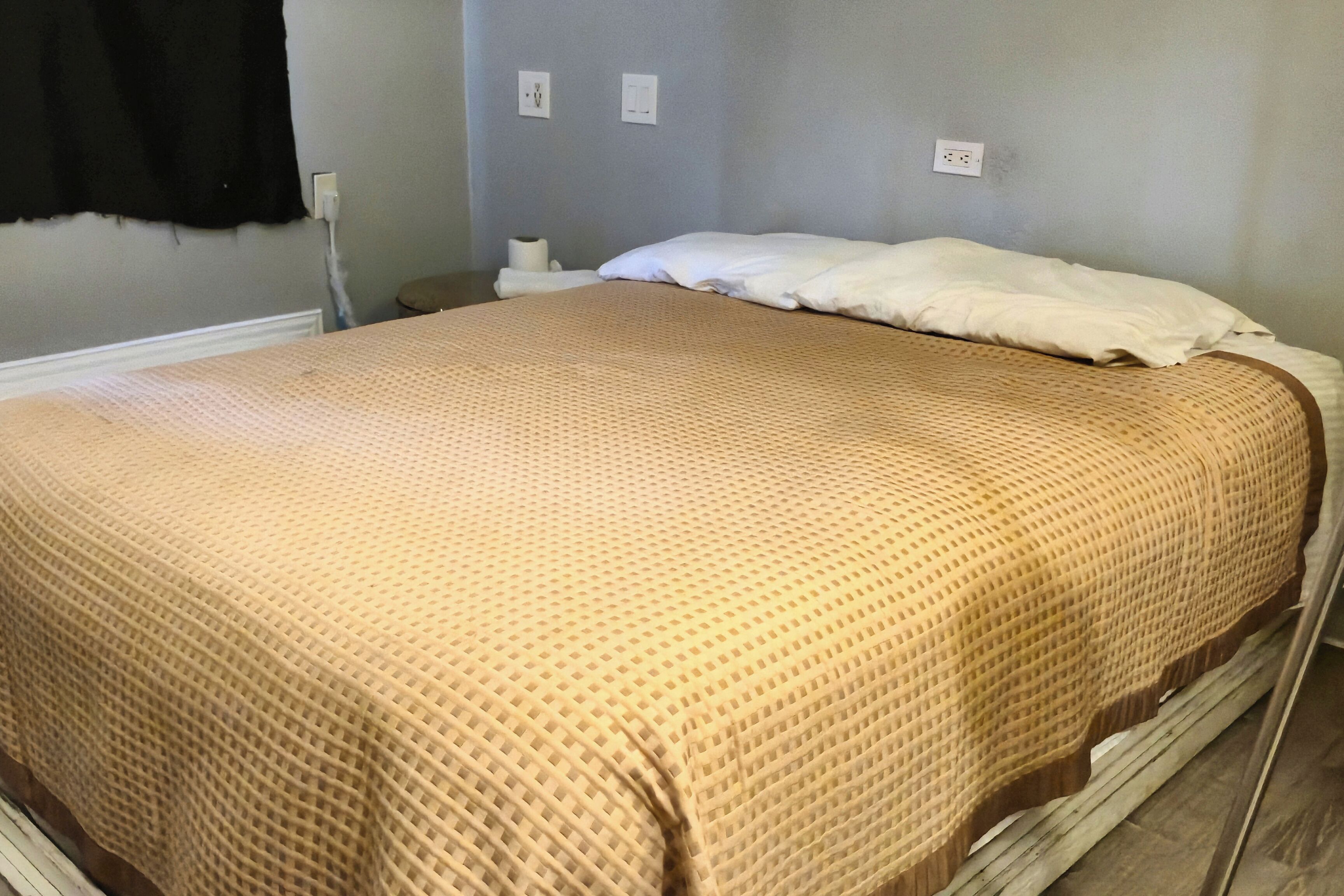 Una cama con una colcha de color beige con estampado, un almohadón blanco y un cabecero de madera.