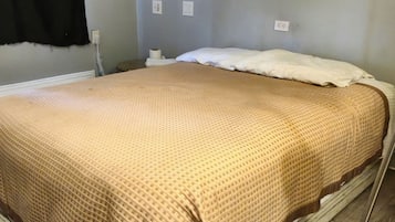 Una cama con una colcha de color beige con estampado, un almohadón blanco y un cabecero de madera.
