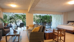 A spacious living area with a sofa, coffee table, and a bed. There is a view of the outdoors through large windows. - Corrales Bay Resort (Los Corrales)
