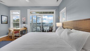 Quarto com uma cama grande, uma escrivaninha e vista para uma marina através de portas de vidro.