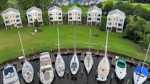 Uma marina com vários barcos atracados, cercada por uma área residencial com casas e um lago ao fundo.