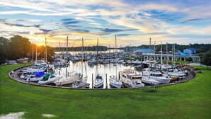 Uma marina com vários barcos atracados, rodeada por zonas verdes e um edifício com telhado azul.