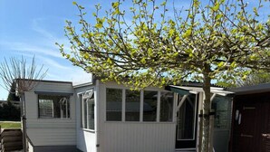 Ein kleines, eingeschossiges Gebäude mit einer Terrasse, die ein Fliesenmuster und einen Baum aufweist.