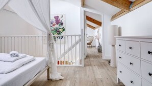 Un dormitorio con cama a dosel, vigas de madera, cómoda blanca y silla de mimbre.