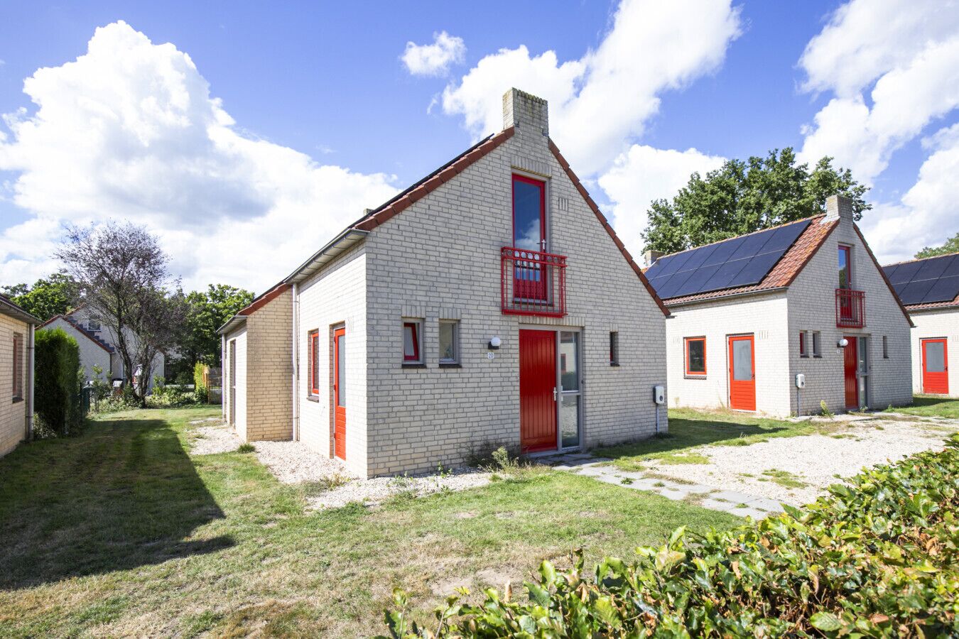 A row of white brick buildings with red doors and windows, surrounded by a grassy area and trees.