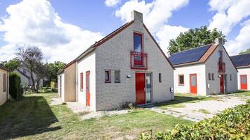 A row of white brick buildings with red doors and windows, surrounded by a grassy area and trees.