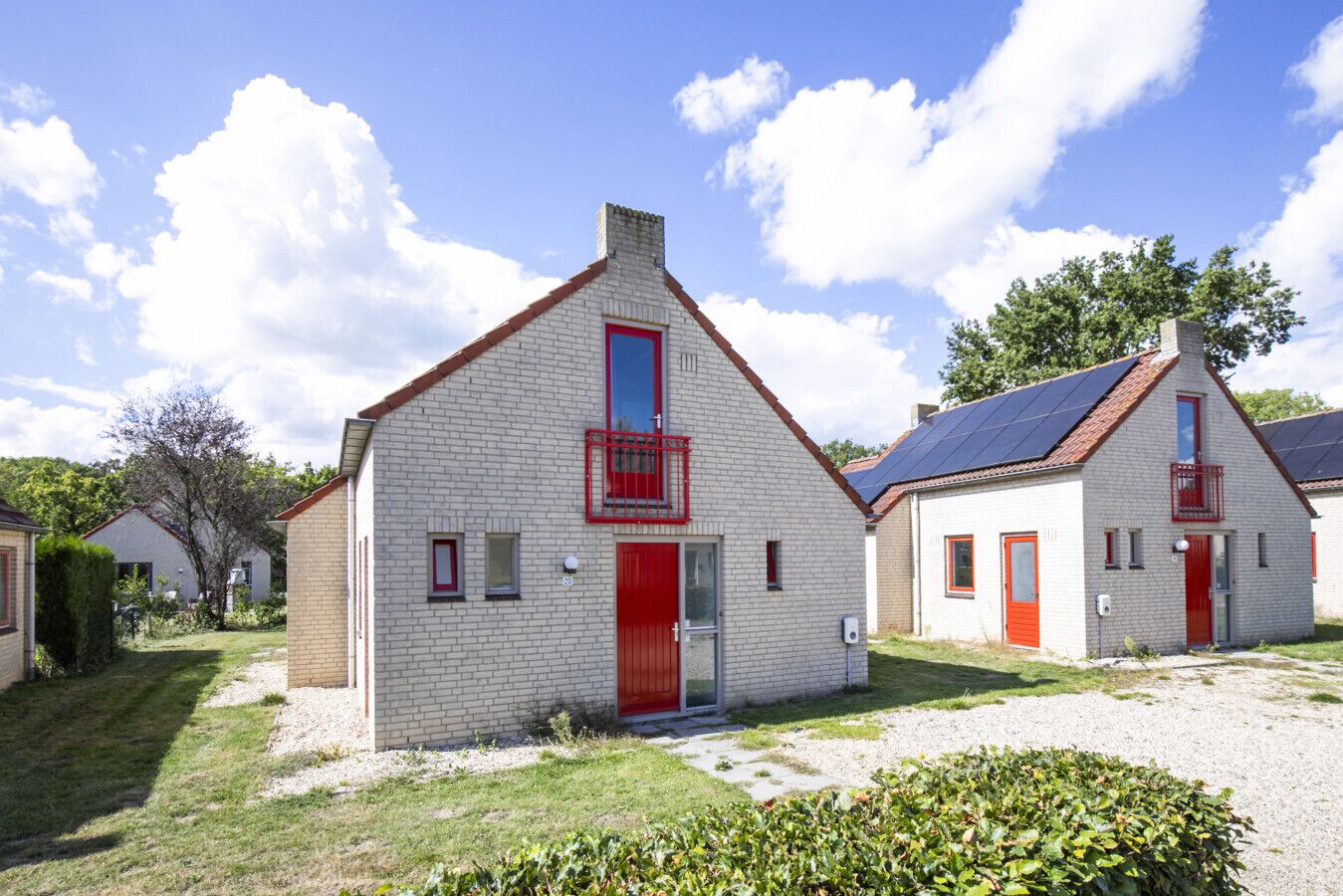 Une rangée de maisons en briques blanches, avec des portes et des fenêtres rouges, chacune dotée d’un petit balcon et de panneaux solaires sur le toit.
