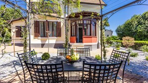 A patio with a table and chairs, surrounded by a garden with various plants and a building in the background. - Luxurious home in Opatija with private swimming pool, can be inside or outside (Opatija)