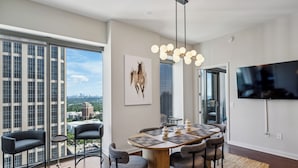 Ein stilvoller Essbereich mit großem Tisch, Stühlen und Blick auf die Stadt durch raumhohe Fenster.