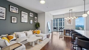 Ein modernes Wohnzimmer mit einer Eckcouch, einem Essbereich mit Barhocker und einem großen Fenster mit Blick auf die Stadt.