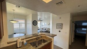 A kitchen with granite countertops, a sink, and wooden cabinets. There is a dining area with a table and chairs visible through an open doorway. - Luxurious Condo 2BD/2BA w/ Pool, Gym, and Sauna (Scottsdale)
