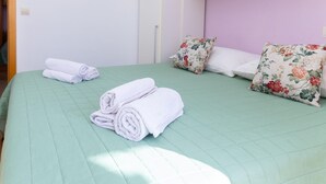 A neatly made bed with a green quilt, two rolled white towels, and floral-patterned pillows.