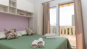 A bedroom with a green bedspread, floral pillows, a white wardrobe, and a balcony with curtains.
