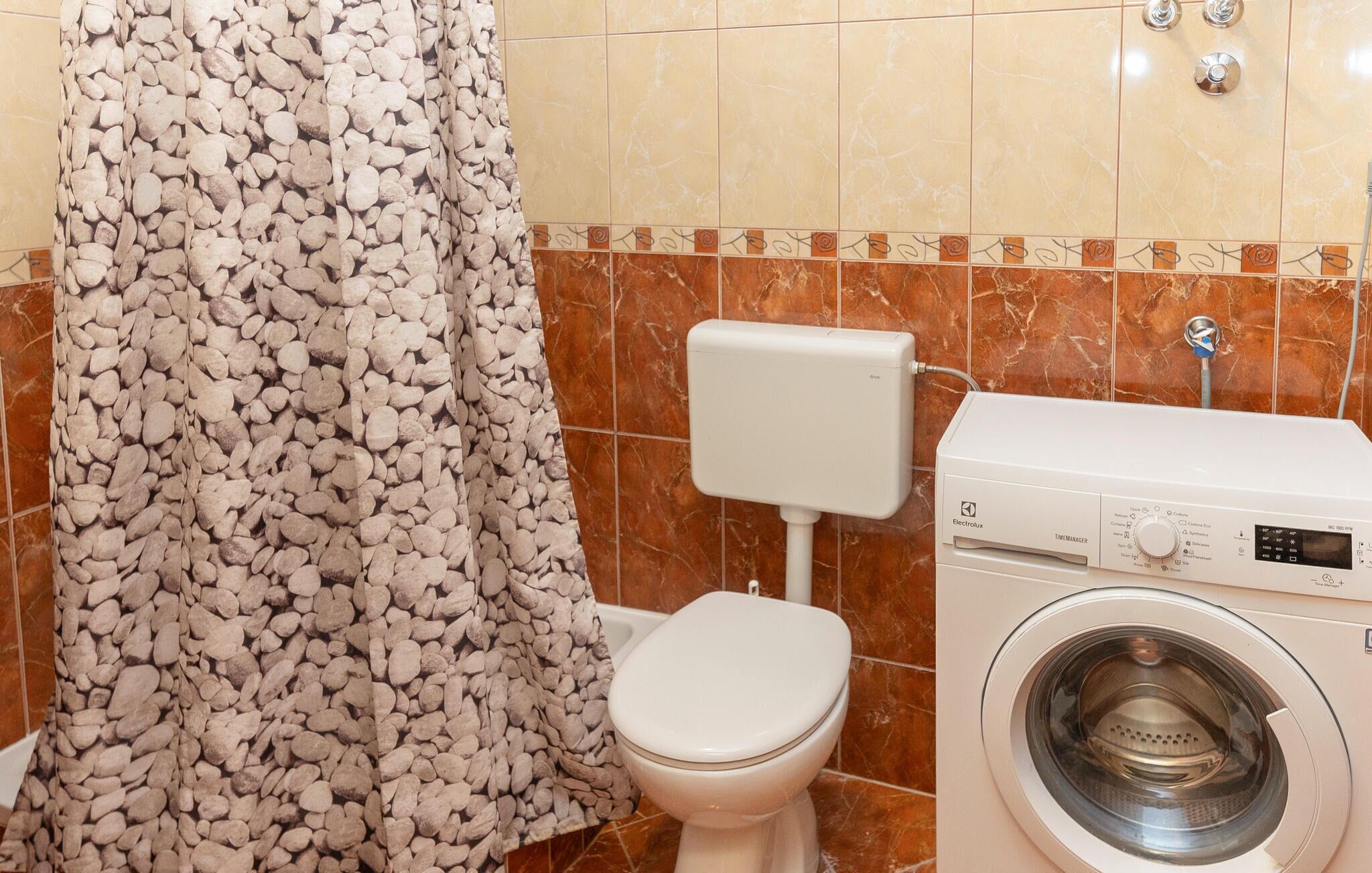 Un baño con inodoro, lavadora y cortina de ducha estampada con motivos de piedras.
