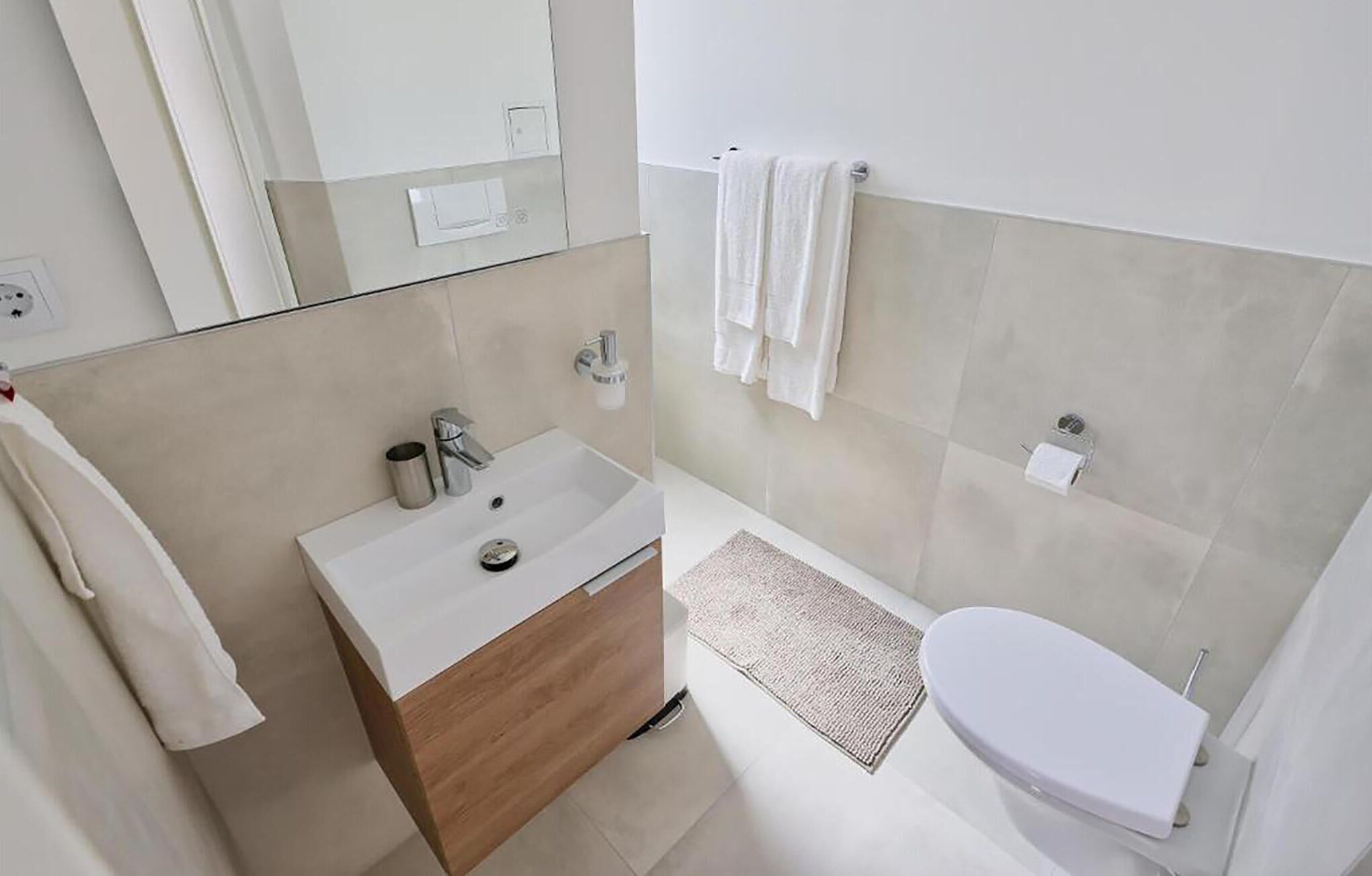 A modern bathroom with a white sink, wooden vanity, and a toilet.