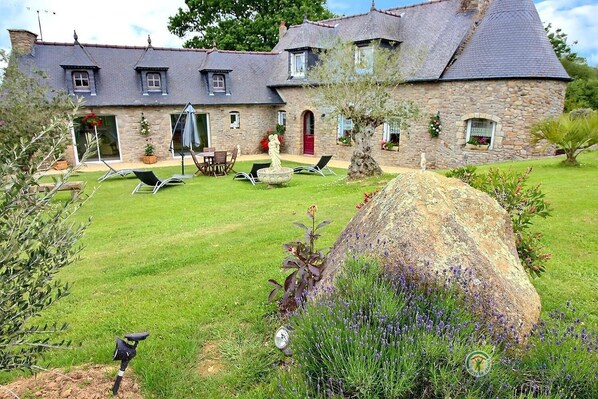 A stone house with a large lawn, outdoor seating, and a prominent rock in the foreground.