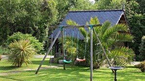 A garden with a swing set, a birdbath, and a house with a sloped roof.